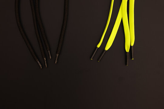 Macro close up framing of neon yellow and solid black shoelaces with metallic aglets positioned adjacent to each other on a dark matte background under indoor studio lighting