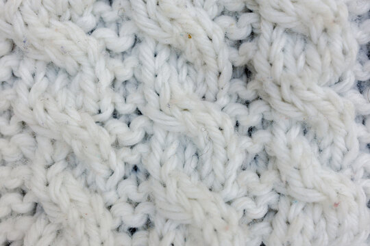 Macro of heavy white chunky yarn forming intricate cable knit patterns serving as a cozy winter textile background asset