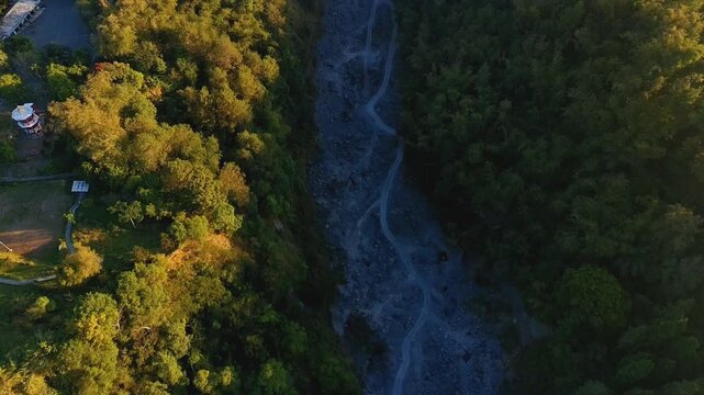 Aerial view of Kaliurang riverbed winding through lush green forest under golden hour light Pakem, Special Region of Yogyakarta, Indonesia.