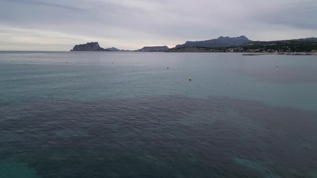 Aerial view of a person on a paddleboard in the calm turquoise sea with the Penon de Ifach in the distance in Moraira, Valencian Community, Spain.