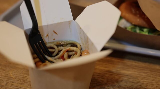 Stir-fried noodles in an open takeaway box with a fork. Asian-inspired fast food meal. Convenient takeout lunch or dinner. Food delivery and casual dining concept. Disposable packaging.