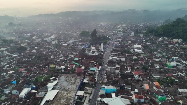 Aerial view of the town of Ciwidey with its central mosque and dense rooftops surrounded by misty hills in Bandung, West Java, Indonesia.