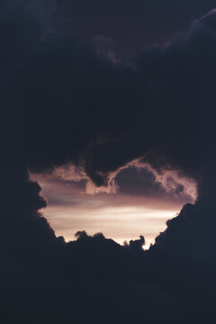 View of dramatic dark storm clouds parting to reveal a soft pink and orange sunset glow in the sky in Merikula, Harju maakond, Estonia.