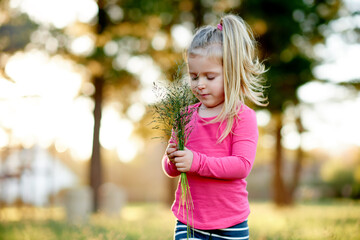 Naklejka premium Park, child and gathering grass for play, holiday and development in environment with bokeh. Outdoor, girl and kid with collection of plants in nature for learning, growth and spring vacation