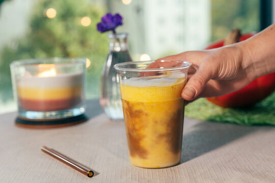 Woman picking up a glass of homemade pumpkin spice latte from an outdoor table in a cozy autumn setting with warm seasonal colors