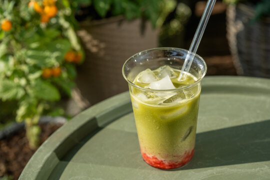 Homemade iced strawberry matcha latte with fresh strawberry layer, milk and green matcha served on a table surrounded by lush garden plants