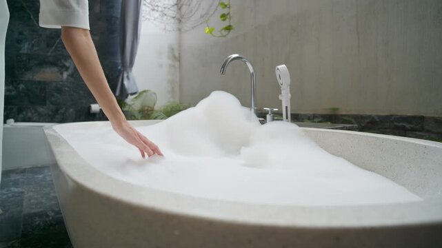 Close up of graceful female hand gently touching foam in stone bathtub in balinese style