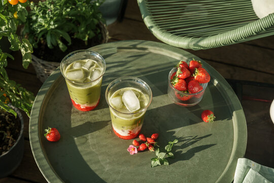 Top view of two refreshing strawberry matcha lattes with fresh strawberries arranged on a sunny outdoor table with generous copy space