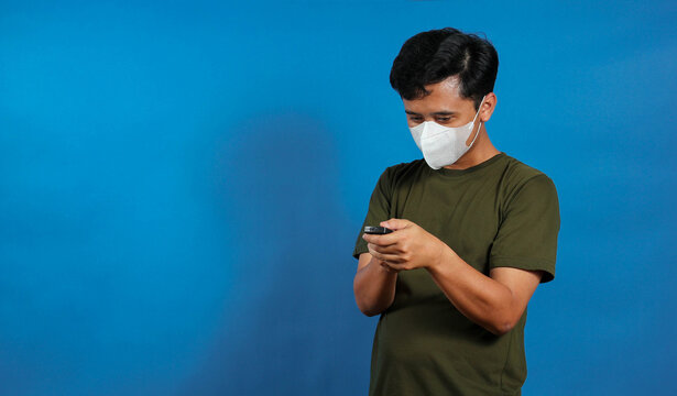 An Asian man wearing a medical mask is opening the TV remote control cover to replace the old batteries with new ones.