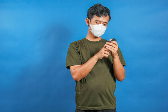 An Asian man wearing a medical mask is opening the TV remote control cover to replace the old batteries with new ones.
