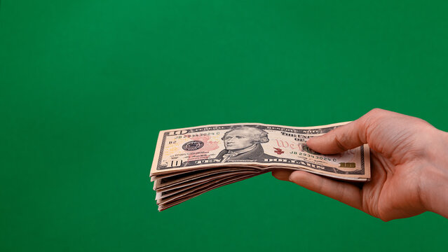 Hand holding a stack of US ten dollar bills isolated on green background with copy space