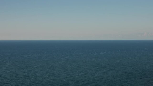 Drone aerial timelapse of clear blue sky split with fast accelerated sea waves from high altitude