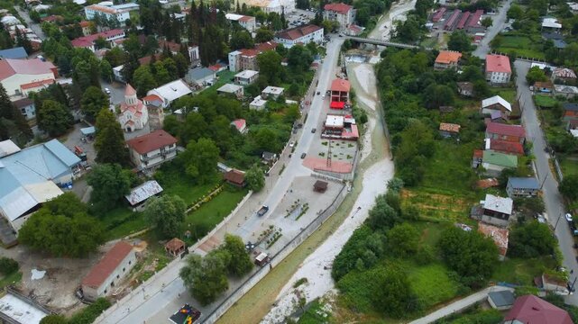 High-altitude perspective of a drone flying over the picturesque town of Ambrolauri in Georgia, capturing the Rioni River waterfront, traditional red-roofed houses, and lush green mountain scenery