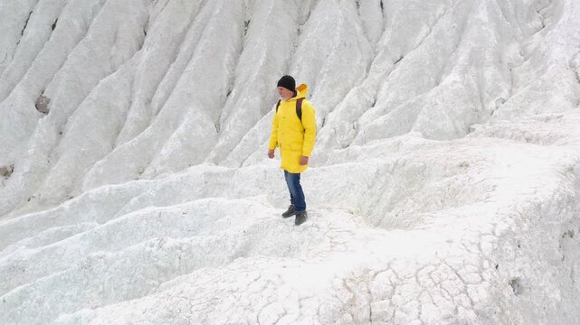 Lonely explorer and outdoor brand adventure, aerial orbit around hiker in yellow jacket with backpack on white chalk hill with eroded slopes. Explorer on summit, drone circles around man