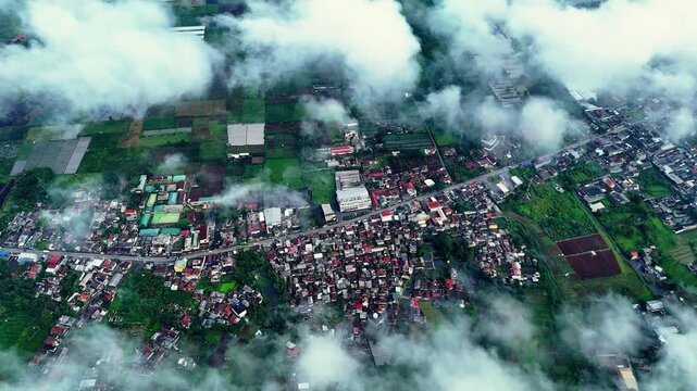 Aerial view of Sukalarang showing residential areas and green agricultural fields partially covered by clouds in Sukabumi, West Java, Indonesia.