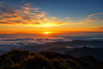 Fototapeta premium Orange horizon above a sea of clouds and rugged peaks