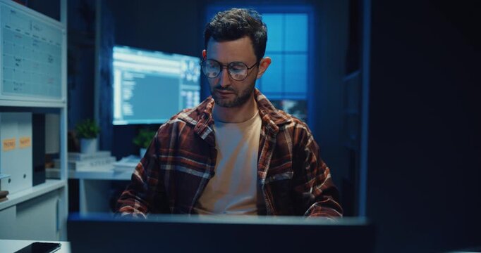 Young Caucasian male programmer write code on computer in home office at late night. AI technology, cybersecurity, software developer, freelance innovation, database system, digital network concept.