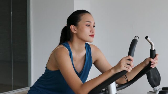 Southeast asian woman in her 20s cycling casually in fitness center, relaxed light workout on maintenance day