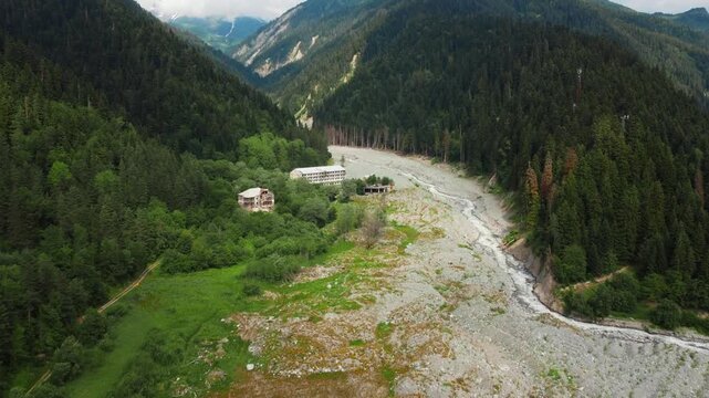 Dramatic aerial photography flying over the remnants of a devastating landslide in Georgia's remote Shovi Racha mountain valley, revealing a wide path of rocks and debris among lush green coniferous f