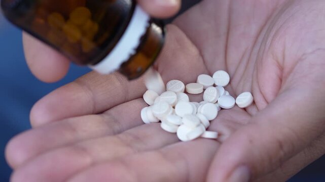 close up woman hand holding a medicine, with pours the pills out of medicine bottle. Stop drug use Taking Medication Caring for the health care medical concept.