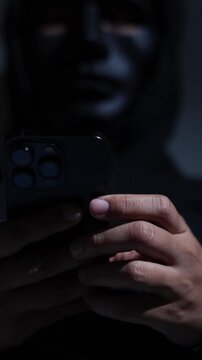 Phone scammers protection, mobile security, wearing black hood sitting in dark.