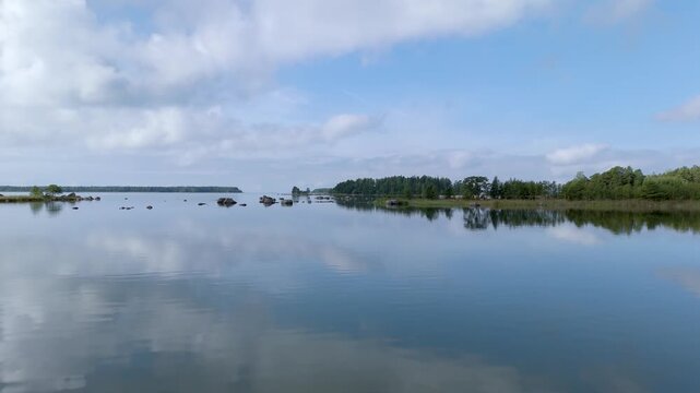 Aerial view of the calm waters of the Gulf of Finland with reflections of the sky and surrounding forest coastline in Hamina, Kymenlaakso, Finland.