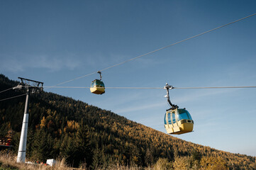 Vibrant cable cars glide effortlessly up a picturesque forested mountain, providing an exhilarating journey through nature's autumnal splendor on a beautiful clear day © Gicu