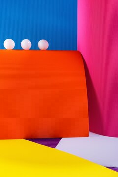 Three white ping pong balls balancing on orange corrugated paper with colorful geometric background