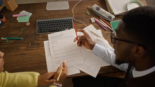 African American male tutor explaining math test to teenage girl from high angle view. Footage fitting for tutoring services, academic coaching promotion, exam preparation marketing