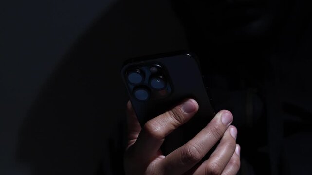 Phone scammers protection, mobile security, wearing black hood sitting in dark.