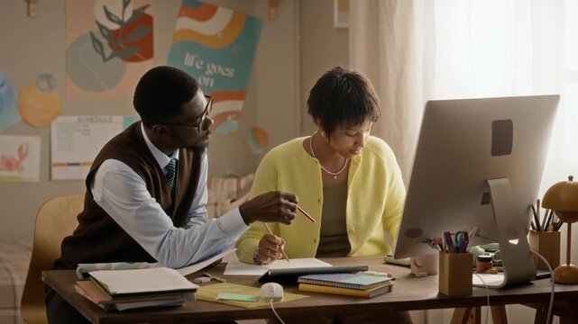 African American male tutor explaining assignment to Black female teenager writing notes at desk. Footage is suitable for private tutoring services and online education marketing campaigns