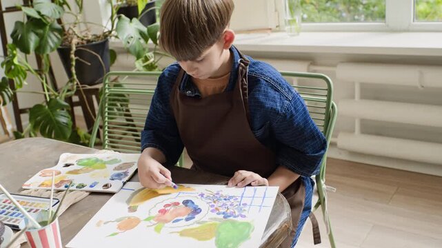 Caucasian boy drawing still life with pastels during creative masterclass while girl paints in foreground. Footage suitable for art school marketing and children education campaigns