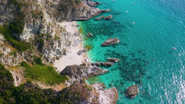 Capo Vaticano Calabria Italy 4k drone view of dramatic jagged rocks and cove. Top down flyover hidden beach with kayaks reveals turquoise sea and rugged coastline panorama pull out shot