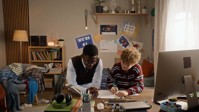 African American tutor assisting Caucasian teenager with homework while writing notes at desk. Clip suits private tutoring promotions and educational campaigns