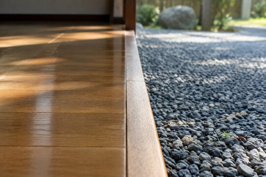 Wooden boundary line dividing polished floorboards from rough gravel.