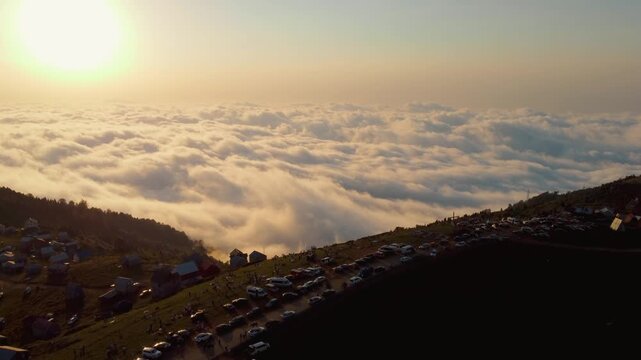 The beautiful landscape of the mountain village of Gomis mta with colorful houses perched on a green hill above a sea of clouds filmed by a drone flying over the settlement during a warm sunset.