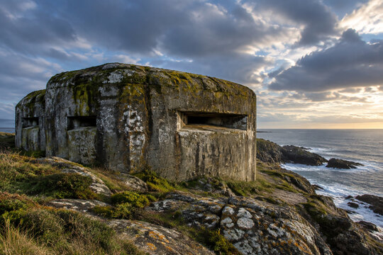 Weathered concrete bunker on a rocky coastline covered in moss.