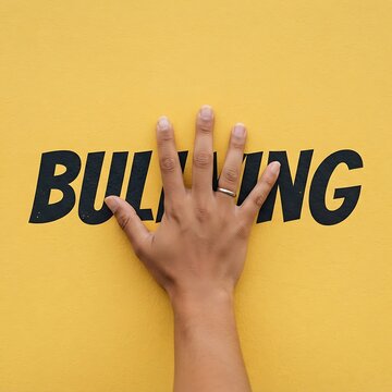 A person placing their hand over the word bullying written in bold black letters on a bright yellow wall, representing a stand against abuse
