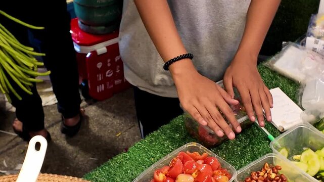 Close up shot of vendor hands closing a clear plastic lid on a takeout container filled with traditional fresh Thai salad at a street food market stall.
