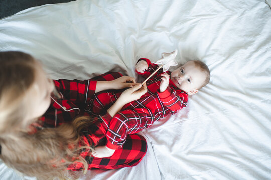 Two children playing in bed wearing red checkered pajamas having fun over Christmas tree at background in room. Winter holiday season.