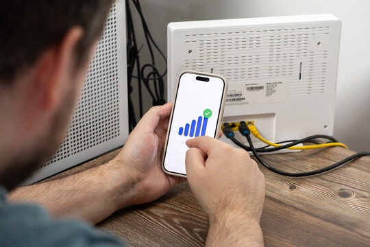 A person checks their strong wifi signal strength on a smartphone app screen next to a home router to ensure reliable network connectivity for remote work and digital management