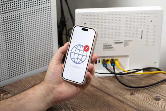 A hand holds a smartphone displaying an internet connection error symbol, highlighting home connectivity issues with a router background to illustrate common technical difficulties