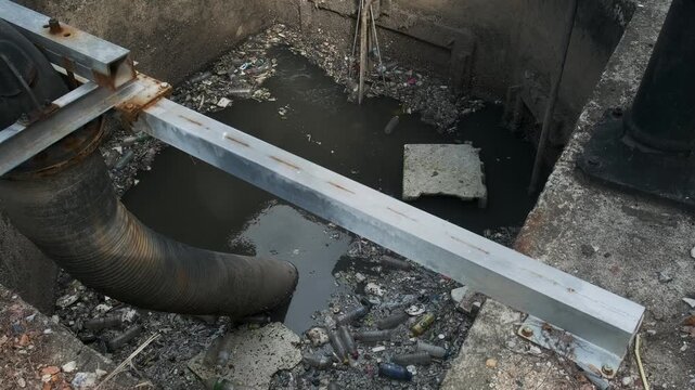 Dirty wastewater containing plastic bottles, floating debris and solid waste collects inside open treatment section at facility in Phuket. Sewage management, water pollution, wastewater treatment