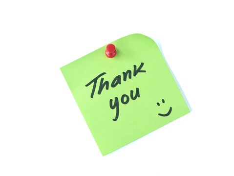 Green adhesive note with handwritten text thank you and a happy face pinned on a white background. Great for appreciation, customer support, gratitude, and friendly business communication concepts