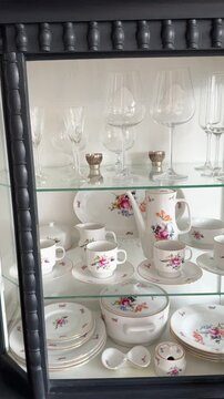 Antique porcelain tableware: a set of plates, cups and saucers, a soup tureen, serving dishes. The set is displayed in a vintage sideboard