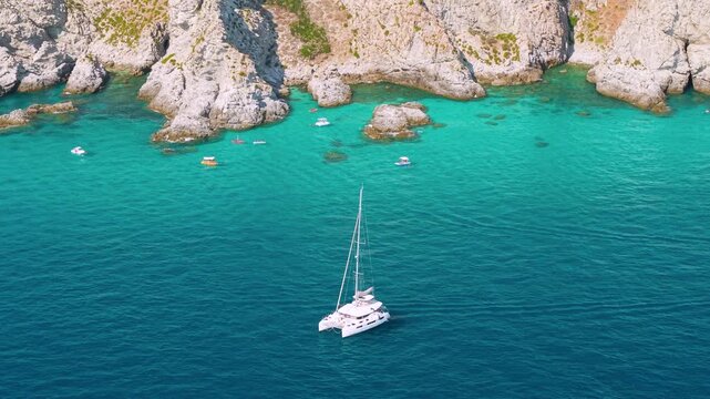 Capo Vaticano Calabria Italy 4k drone view of luxury catamaran yacht anchored. Near dramatic cliffs on crystal clear turquoise sea, exclusive sailing vacation lifestyle broll establishing shot