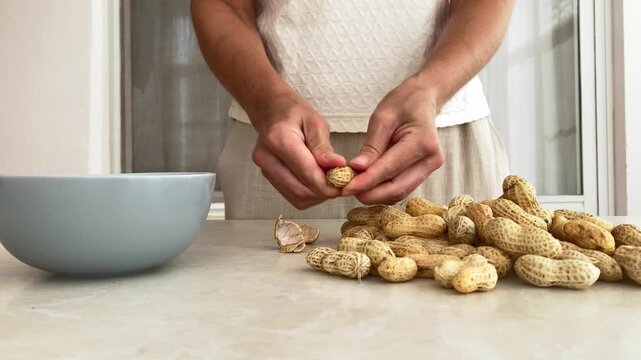 A woman is peeling fresh peanuts, a natural product of plant origin. The concept of vegetarian nutrition, natural products, and a varied plant‑based diet