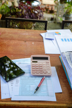 Tax accounting and financial planning with calculator, 1040 form, and smartphone on wooden desk. Report, paperwork, pencil, and binder clip in business workspace-vertical image.