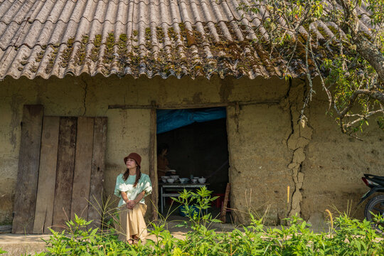 Woman standing beside old mud-brick house doorway, Y Ty, Lao Cai, Vietnam