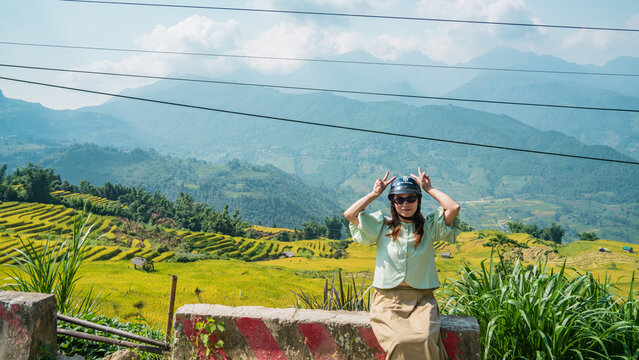 Woman playfully posing with helmet above golden rice terraces, Y Ty, Lao Cai, Vietnam